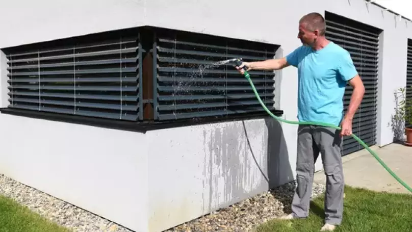 Mann reinigt Außenjalousien mit Wasser