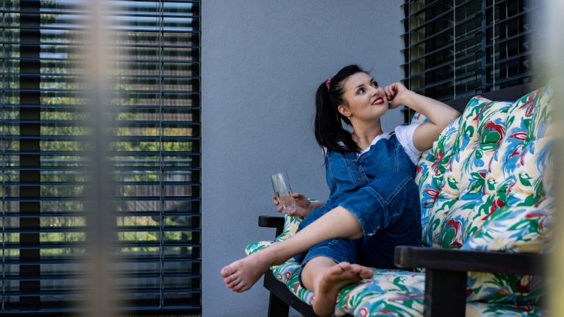 Fenster mit Außenjalousien_Frau auf dem Sofa auf der Terrasse